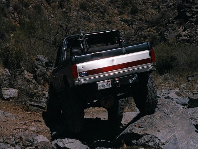Topless Ford Bronco climbing desert boulders, rear view of striped tailgate