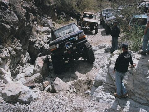 1989 Ford Bronco - Several off-road vehicles tackle a challenging rocky path, with onlookers observing the difficult terrain.