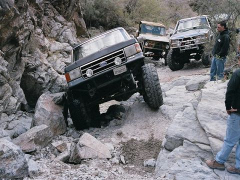 1989 Ford Bronco - Several off-road vehicles tackle a challenging rocky terrain in a desert environment.