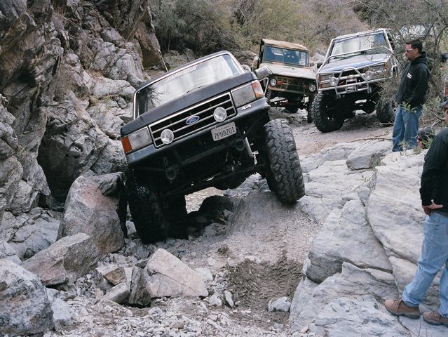 Dark lifted Ford Bronco climbing boulders in a rocky canyon trail