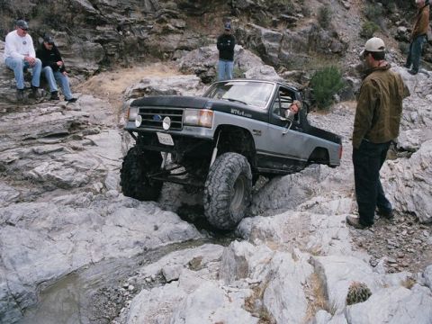1989 Ford Bronco - A heavily modified Ford Bronco navigates a rocky off-road trail with onlookers observing the action.