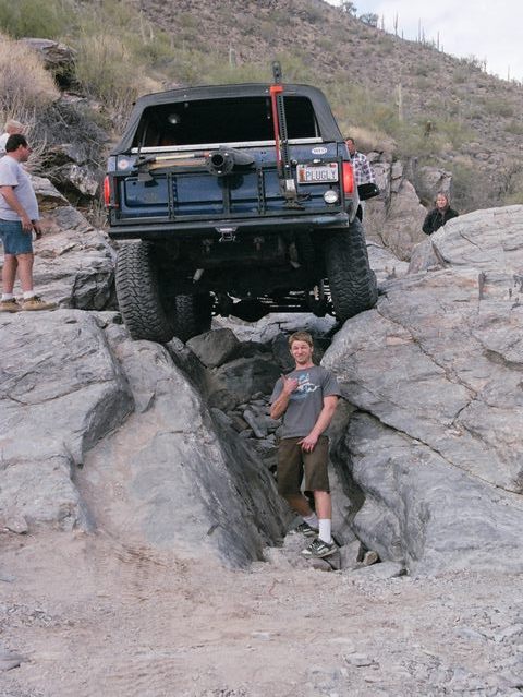 1989 Ford Bronco - A blue Ford Bronco is shown off-roading on a rocky trail, with a person standing nearby.