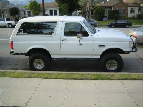 1990 Ford Bronco - white lifted full-size Ford Bronco with a hardtop sits at a residential curb on chunky tires and styled wheels.