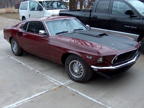 1969 Ford Mustang - A maroon 1969 Ford Mustang is parked on a concrete surface next to a white van and a black pickup truck.
