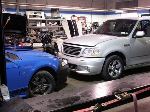 2001 Mercury Grand Marquis - Two performance vehicles, a Ford F-150 SVT Lightning and a Ford Mustang, are parked in a workshop with their hoods open.