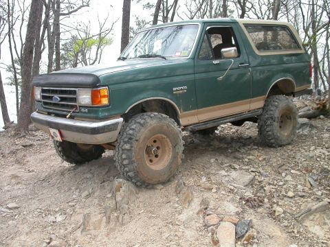 1990 Ford Bronco - This modified Ford Bronco navigates a challenging rocky terrain with its lifted suspension and aggressive tires.