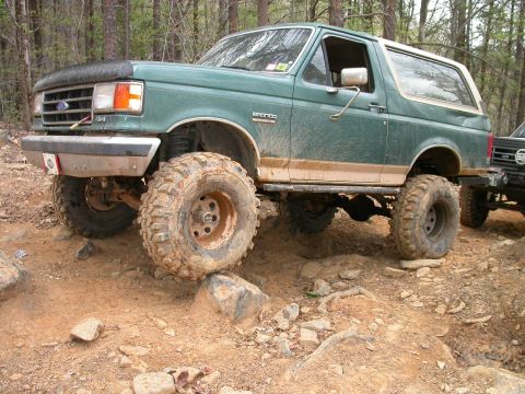 1990 Ford Bronco - This 1990 Ford Bronco is shown off-roading on a dirt trail with large tires and lifted suspension.