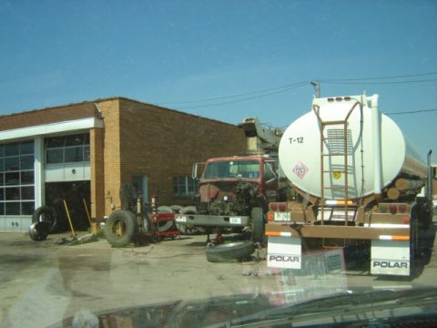 1992 Ford Bronco - A tanker truck and a truck chassis are parked outside a garage, suggesting repair or maintenance work.