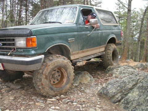 1990 Ford Bronco - A green 1990 Ford Bronco tackles a challenging rocky trail with its driver visible.