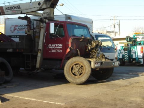 1992 Ford Bronco - A red truck with a crane attachment and exposed engine sits in a lot, with other vehicles visible in the background.