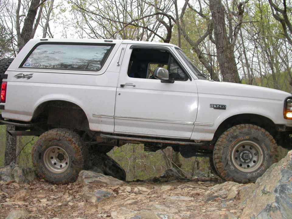 White Ford Bronco on rocks, 4x4 sticker on rear quarter panel, 'BRONCO' badge on fender