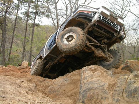 1990 Ford Bronco - This modified truck is navigating a challenging rocky terrain with its tires angled on the obstacles.