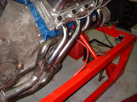 1971 Ford Mustang - Close-up of an engine's exhaust headers and valve covers, mounted on a red stand.