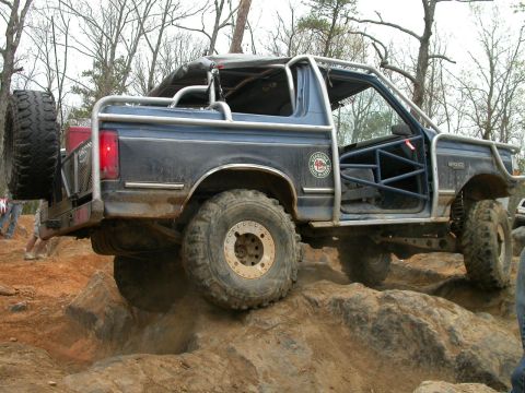 1990 Ford Bronco - Modified blue SUV navigates a rocky trail with its doors removed and a roll cage installed.
