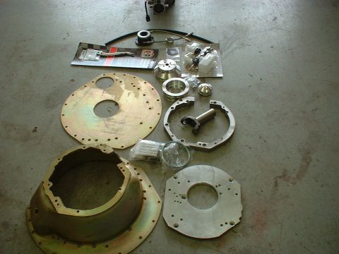 1971 Ford Mustang - Collection of automotive parts, including a bell housing, adapter plates, and clutch components, arranged on a concrete surface.