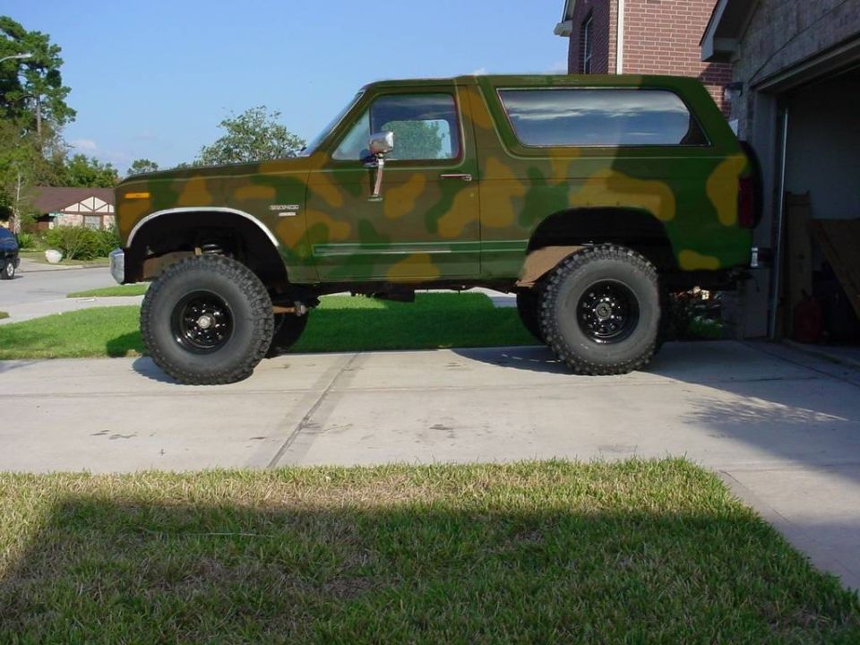 Camouflage-painted lifted Ford Bronco with big off-road tires, side view in a driveway