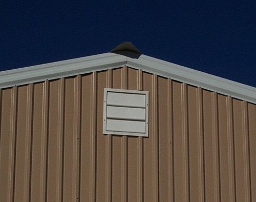 Gable end of tan metal shop building with white louvered vent against blue sky