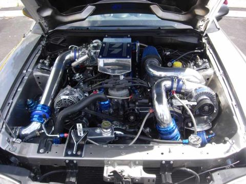1998 Ford Crown Victoria - modified engine bay packed with polished intercooler piping, blue fittings, twin turbos, and a chrome alternator.