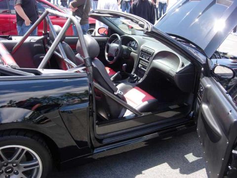 1998 Ford Crown Victoria - Open door view of a black Mustang convertible interior with a chrome roll bar and red-and-black two-tone seats.