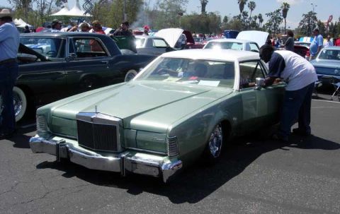 1998 Ford Crown Victoria - metallic green vintage Lincoln Continental coupe with a white roof sits at a crowded outdoor car show as a man leans into its open door.