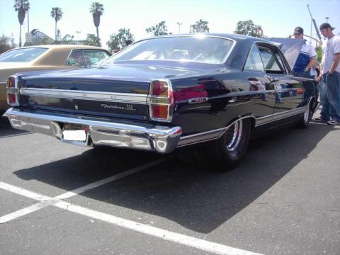 1998 Ford Crown Victoria - dark blue Ford Fairlane 500 sedan is shown from the rear three-quarter, its chrome bumper and badging catching the sun at a show.