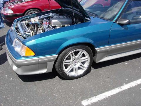 1998 Ford Crown Victoria - teal Fox-body Mustang GT with a dressed-up engine bay sits hood-up on silver wheels, its lower body painted silver-gray.