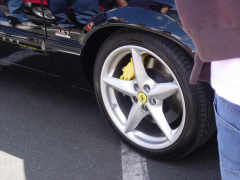 1998 Ford Crown Victoria - black car badged 347 rides on a five-spoke wheel bearing a Ferrari emblem and a yellow brake caliper, shot at close range.