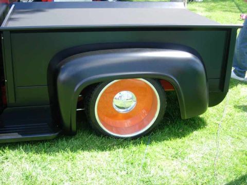1998 Ford Crown Victoria - black rear bed of a custom hot-rod pickup sits on grass, fender flared over an orange-painted smoothie wheel with chrome cap.