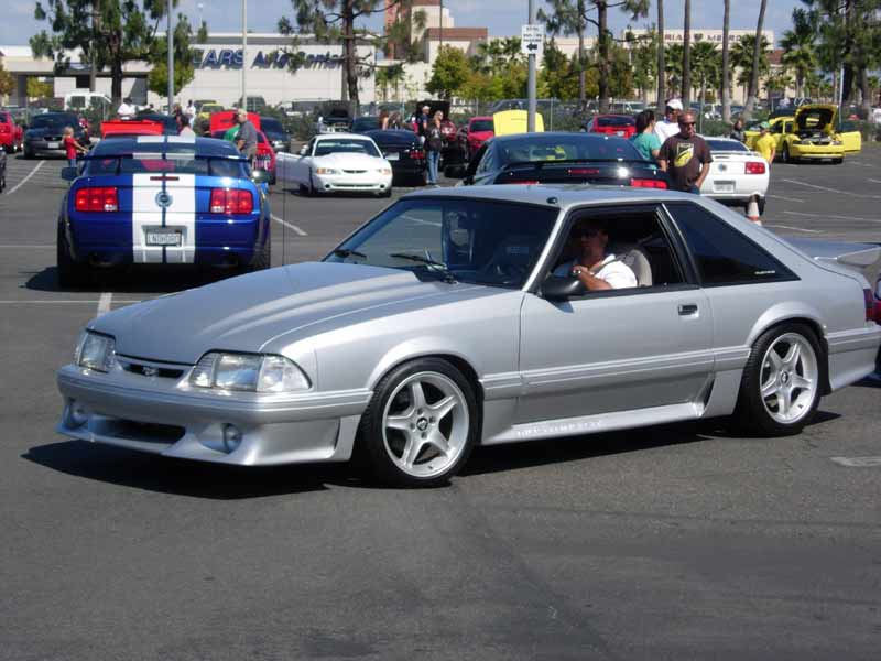 Silver Fox-body Mustang GT driving in car-show lot, front three-quarter