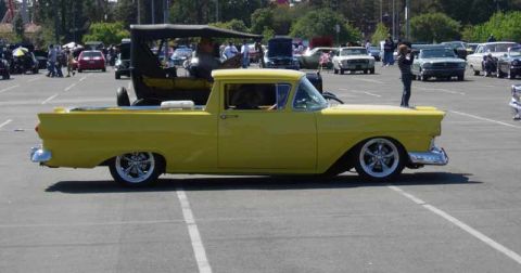 1998 Ford Crown Victoria - yellow customized Ford Ranchero with chrome wheels sits in profile in a parking lot, with a Model T and other cars behind.