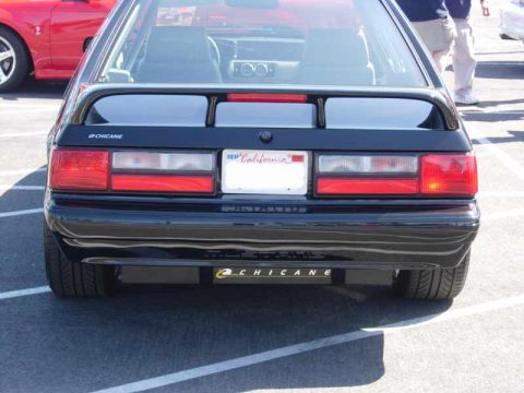 1998 Ford Crown Victoria - rear of a black Fox-body Mustang hatchback shows a wing, California plate, and Chicane badging on the bumper.