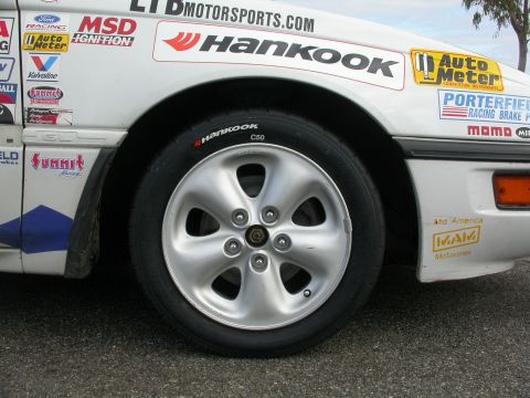 1990 Ford Probe - A white race car is shown from the side, Hankook tires and numerous sponsor decals on its body.