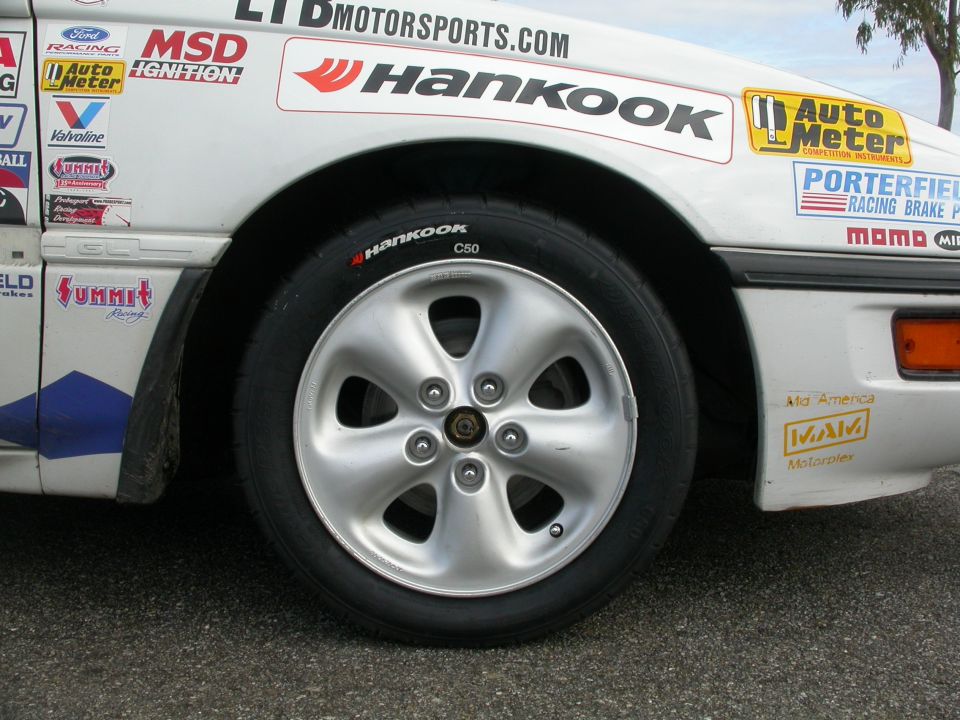 Sponsor-decaled white race car front wheel with Hankook C50 tire on silver five-spoke wheel