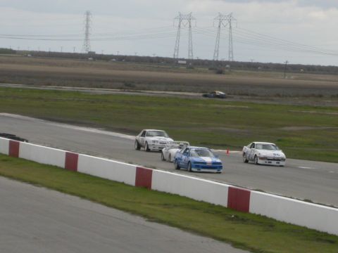 1990 Ford Probe - Multiple cars compete on a race track under a cloudy sky.