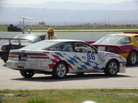 1990 Ford Probe - A white race car with red, white, and blue checkered graphics and the number 86 is parked on a racetrack.