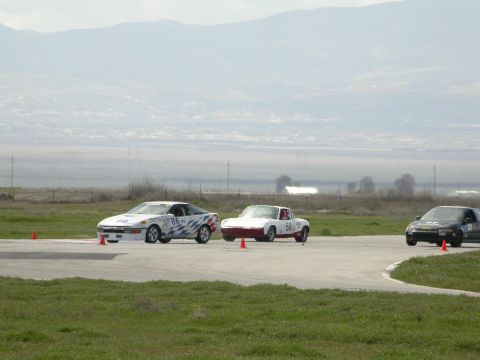1990 Ford Probe - Three cars race on a track with mountains in the background.