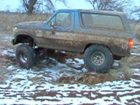 1985 Ford Bronco - Muddy SUV with lifted suspension navigates snowy, off-road terrain.