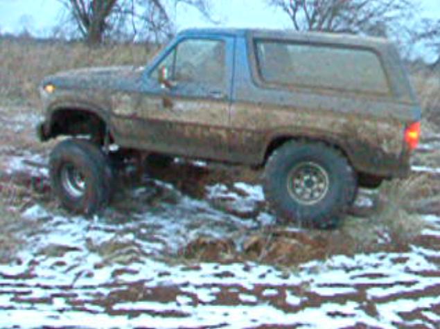 Mud-covered SUV with lifted suspension driving off-road in snow and mud. Blue top, brown body
