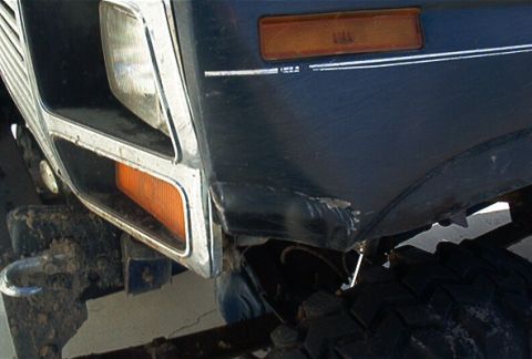 1986 Ford Bronco - Close-up of the front corner of a dark blue SUV, revealing the headlight and turn signal assembly.