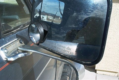 1986 Ford Bronco - The side mirror of a vehicle displays the warning text "Objects in mirror are closer than they appear".