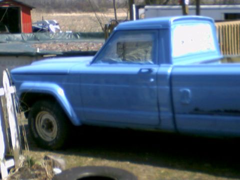 1978 Ford Bronco - A blue pickup truck is parked outside next to a white fence and a red shed.