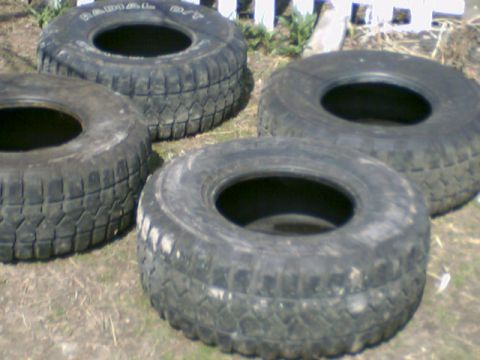 1978 Ford Bronco - set of four worn off-road all-terrain radial tires resting on the ground outdoors.