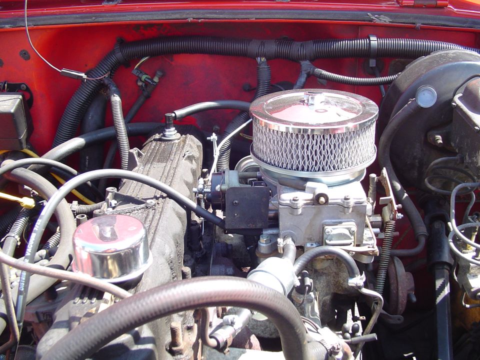 Engine bay of a red 4x4 with a carbureted inline engine and chrome round air cleaner
