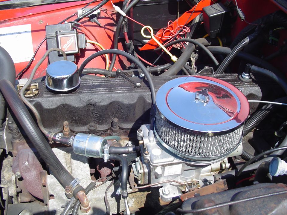Engine bay with chrome air cleaner over carburetor, black valve cover and red Mallory ignition box