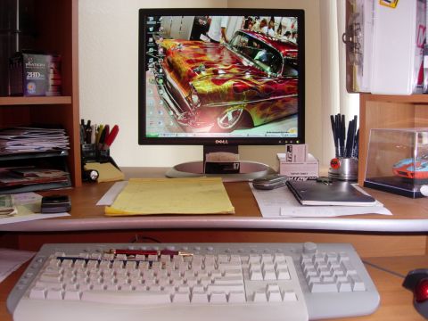 1998 Ford Crown Victoria - Dell flat-panel monitor on a desk shows a flame-painted classic car as wallpaper, flanked by keyboard, pens and papers.