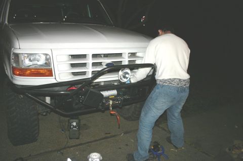 1995 Ford Bronco - A person works on the front of a white Ford Bronco, which has a winch mounted on its custom bumper.