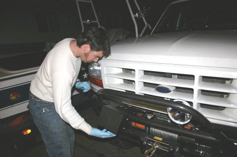 1995 Ford Bronco - Man installs a winch on the front bumper of a white truck, which appears to be from the early to mid-1990s.