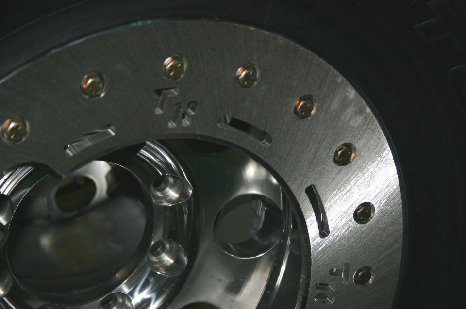 Close-up of a polished metal wheel with gold lug nuts and a black tire. Text 'Tx' is visible