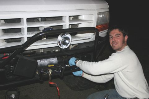 1995 Ford Bronco - A man is installing a winch on the front bumper of a white truck, which appears to be from the mid-1990s.