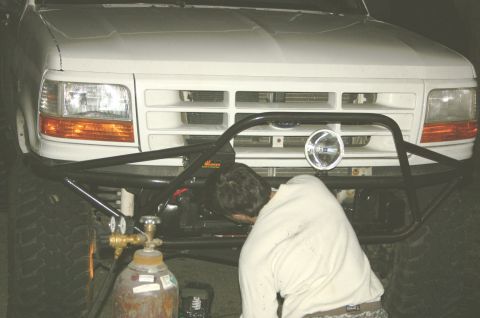 1995 Ford Bronco - A person works on the front end of a white 1995 Ford Bronco, which features a custom bumper with a spotlight.